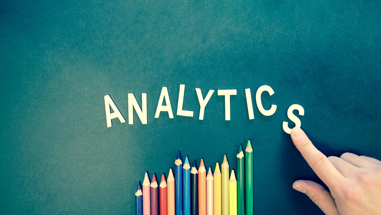 why-choose-us Colored pencils and letters spelling 'ANALYTICS' on a textured background with a hand.